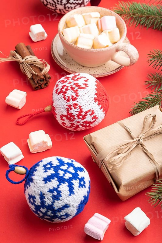 Christmas or New Year composition. Decorations, box, cinnamon, knitted balls, fir and spruce branches, cup of coffee, on a red paper background. Side view, close up
