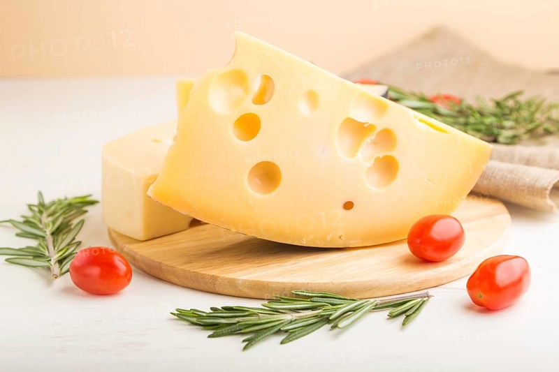 Various types of cheese with rosemary and tomatoes on wooden board on a white wooden background and linen textile. Side view, close up, selective focus