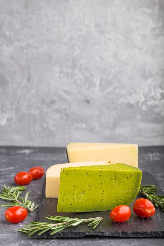 Green basil cheese and various types of cheese with rosemary and tomatoes on black slate board on a black concrete background. Side view, close up, copy space, selective focus