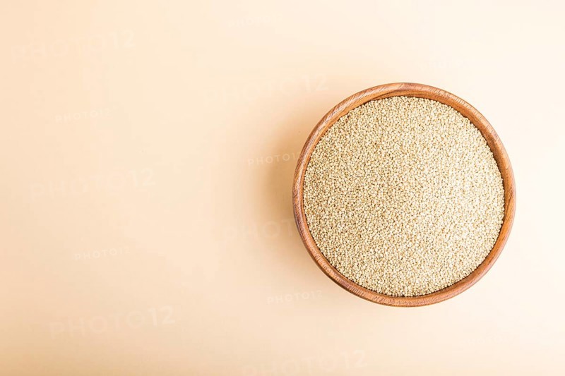 Wooden bowl with raw white quinoa seeds on a pastel orange background. Top view, flat lay, copy space