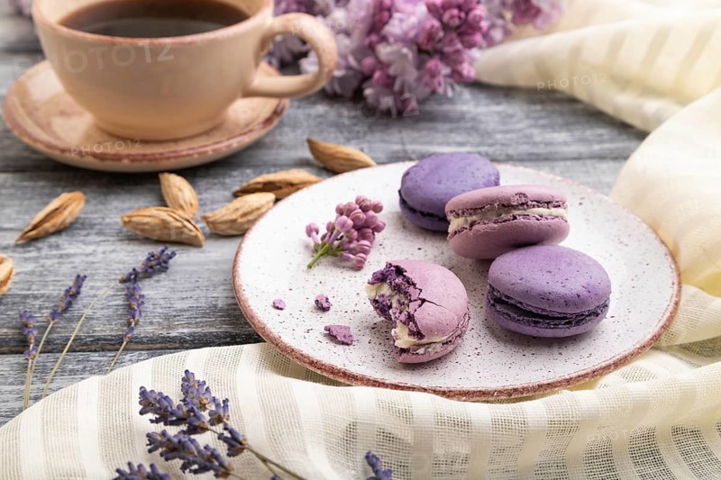 Purple macarons or macaroons cakes with cup of coffee on a gray wooden background and white linen textile. Side view, close up