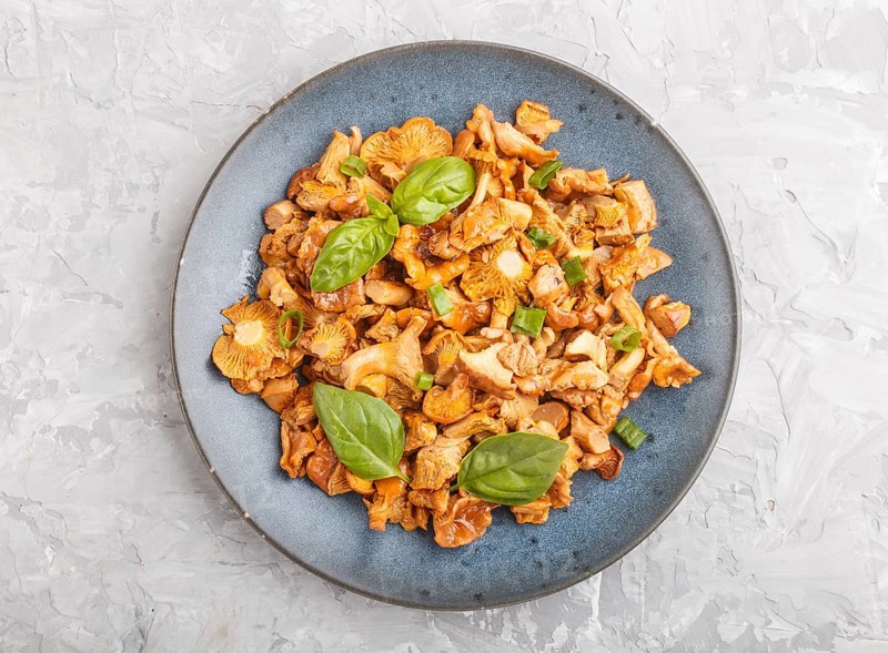 Fried chanterelle mushrooms with basil and spice herbs on gray concrete background. Top view, flat lay