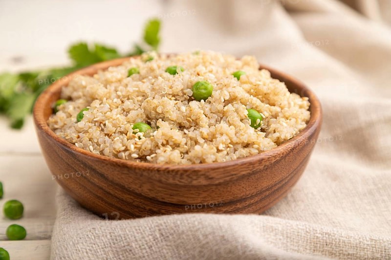 Quinoa porridge with green pea in wooden bowl on a white wooden background and linen textile. Side view, close up, selective focus
