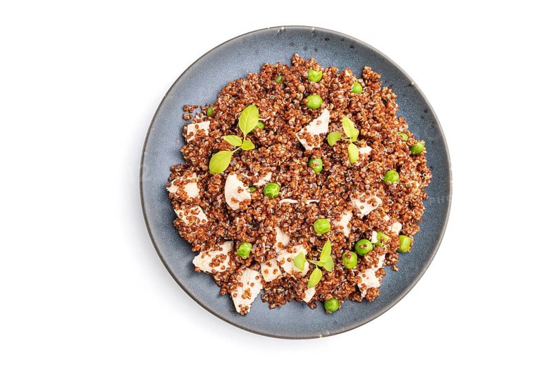 Quinoa porridge with green pea and chicken on ceramic plate isolated on white background. Top view, close up