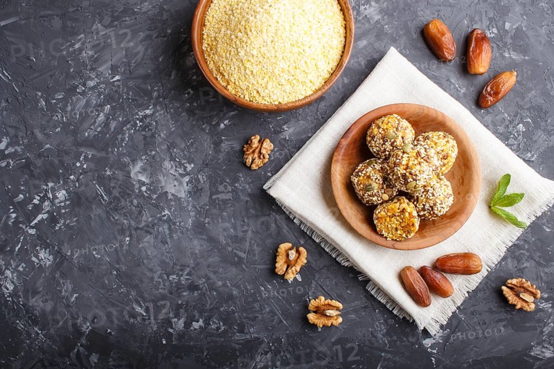 Energy ball cakes with dried apricots, sesame, cornflakes, linen, walnuts and dates with green mint leaves in a wooden bowl on a black concrete background. linen napkin, top view, copy space, flat lay. vegan homemade candy
