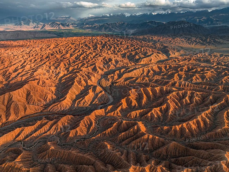 Landscape of eroded hills, badlands at sunset, mountain peaks of the Tian Shan Mountains in the background, aerial view, Canyon of the Forgotten Rivers, Issyk Kul, Kyrgyzstan, Asia