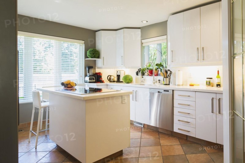 White cabinets, quartz countertop and island with glass cooktop and high back bar stool in kitchen inside a luxurious residential home, Quebec, Canada, North America