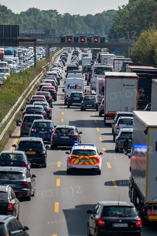 Emergency ambulance with flashing blue lights and siren working its way through a traffic jam on the A3 motorway, over 8 lanes, in both directions, in front of the Leverkusen motorway junction looking north, Friday afternoon heavy traffic, delays due to the traffic jam, Leverkusen, North Rhine-Westphalia, Germany, Europe