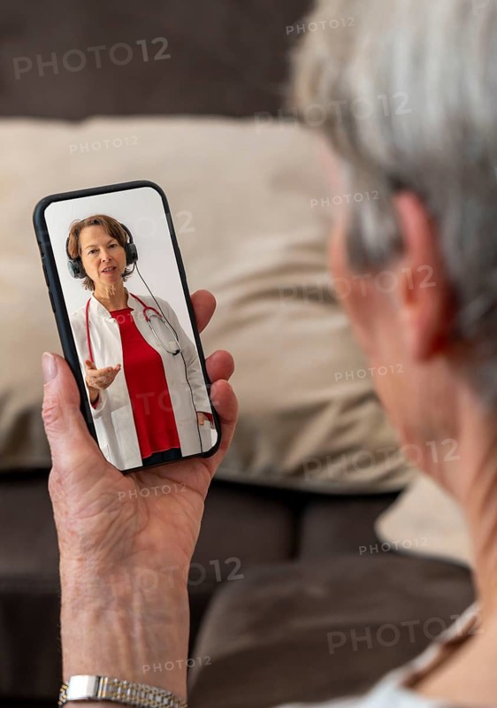Symbolic image of telemedicine, patient speaks to a doctor in a video conference from home via mobile phone, smartphone