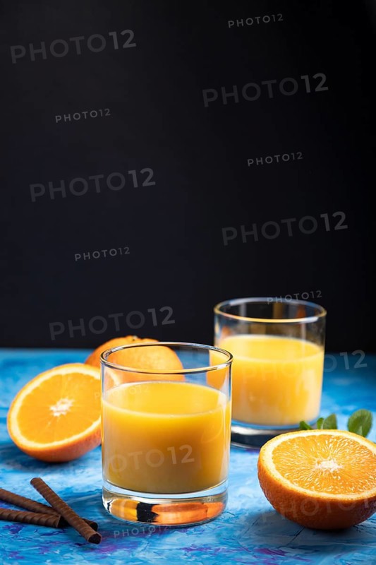 Glass of orange juice on a black and blue background. Hard light, contrast. Side view, copy space