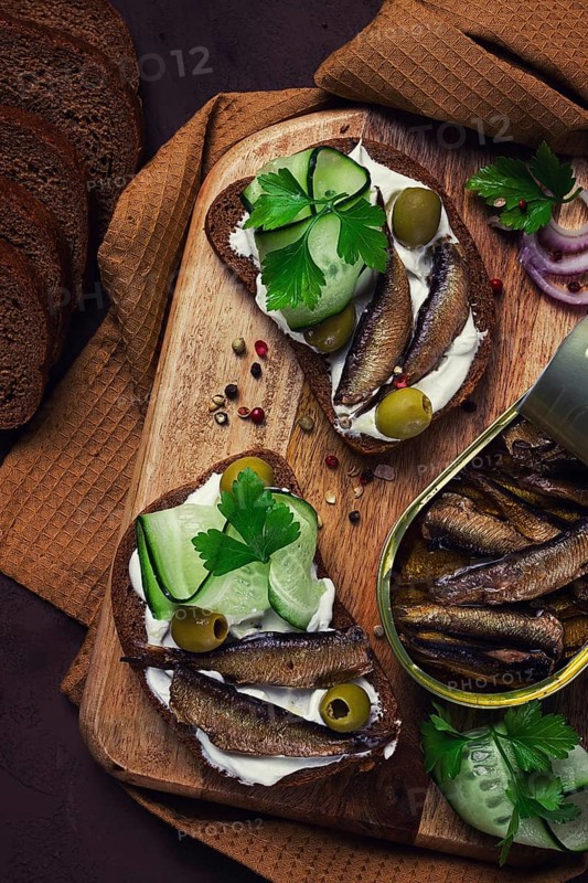 Sandwiches, black bread with sprats, cream cheese, cucumbers, on a cutting board, top view, close-up, no people