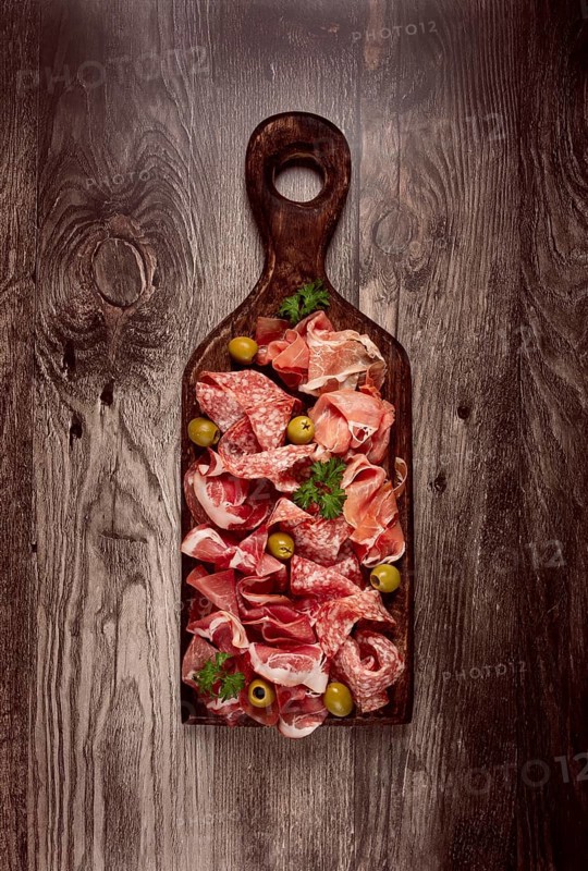 Assortment, sliced meat appetizer, prosciutto, salami and ham, with olives, on a wooden board, breakfast, top view, close-up, no people