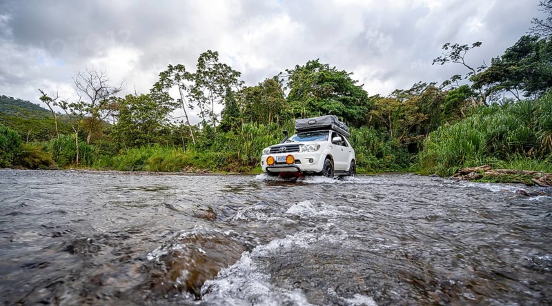 Toyota off-road vehicle with roof tent drives through a wide river in the rainforest, Alajuela province, Costa Rica, Central America