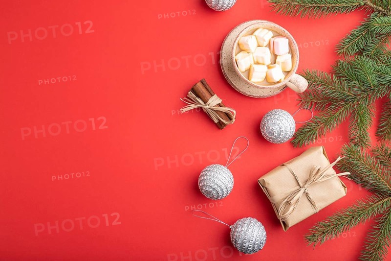 Christmas or New Year composition. Decorations, box, cinnamon, silver balls, fir and spruce branches, cup of coffee, on a red paper background. Side view, copy space