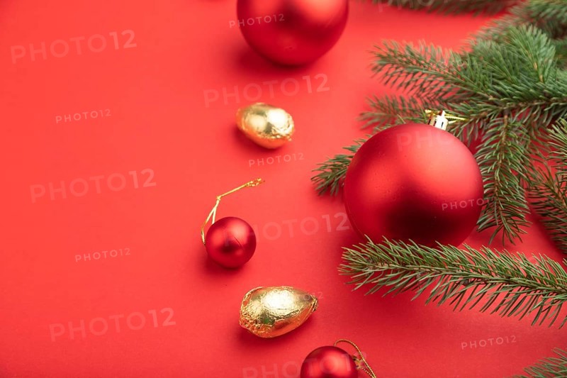 Christmas or New Year composition. Decorations, red balls, fir and spruce branches, on a red paper background. Side view, copy space, selective focus