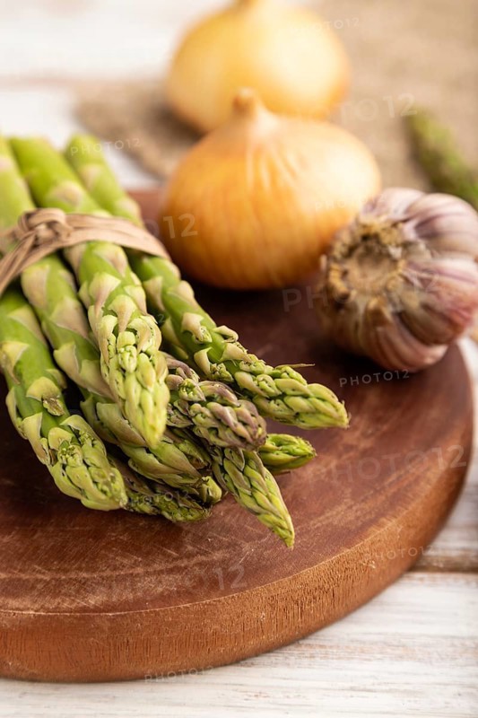 Bunch of fresh green asparagus, garlic, onion on white wooden background. Side view, selective focus. harvest, healthy, vegan food, concept