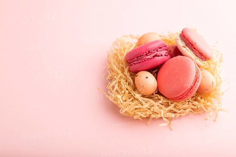 Purple and pink macaroons and chocolate eggs in decorative paper nest on pink pastel background. side view, copy space, still life. Breakfast, morning, easter concept