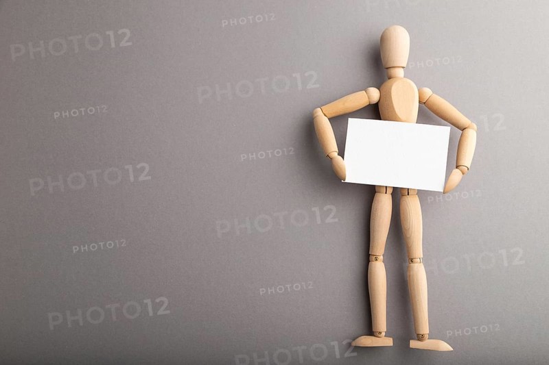 Wooden mannequin holding blank poster on gray pastel background. copy space, isolated, presentation concept