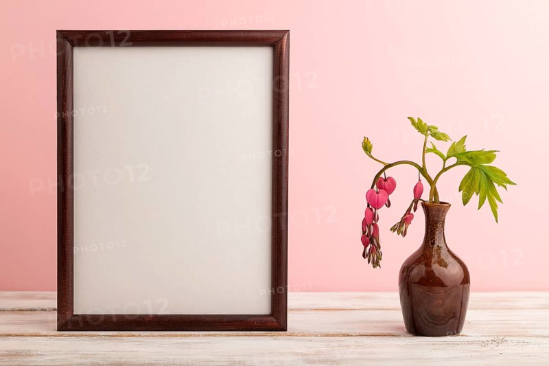 Wooden frame with pink dicentra, broken heart in ceramic vase on pink pastel background. side view, copy space, mockup, template, spring, summer minimalism concept