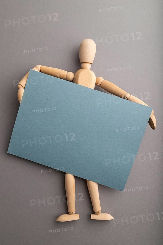 Wooden mannequin holding blue blank poster on gray pastel background. copy space, isolated, presentation concept