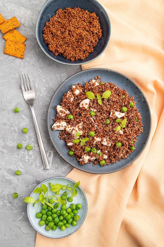 Quinoa porridge with green pea and chicken on ceramic plate on a gray concrete background and orange textile. Top view, flat lay, close up