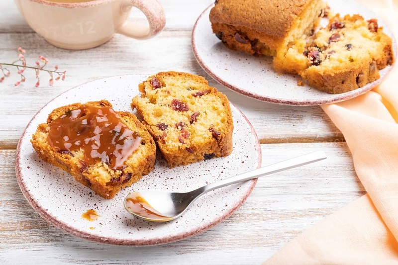 Homemade cake with raisins, almonds, soft caramel and a cup of coffee on a white wooden background and orange linen textile. Side view, close up