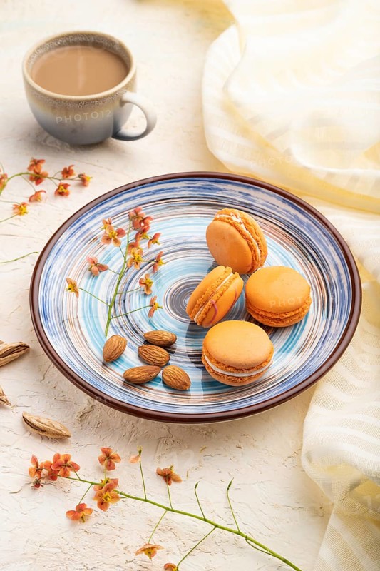 Orange macarons or macaroons cakes with cup of coffee on a white concrete background and linen textile. Side view, close up