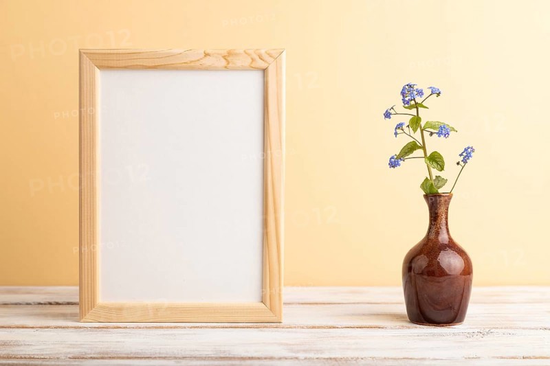 Wooden frame with blue forget-me-not flowers in ceramic vase on orange pastel background. side view, copy space, still life, mockup, template, spring, summer minimalism concept