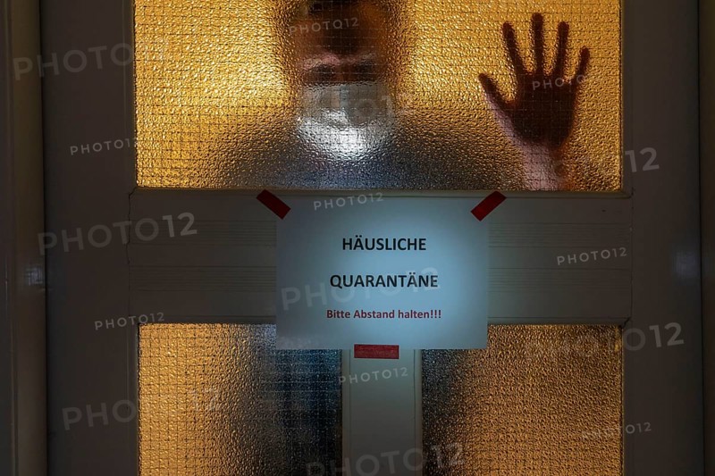 Symbolic image Domestic quarantine, man is in isolation at home due to a suspected corona infection, warning sign for visitors on the front door, communicating with a visitor through the door