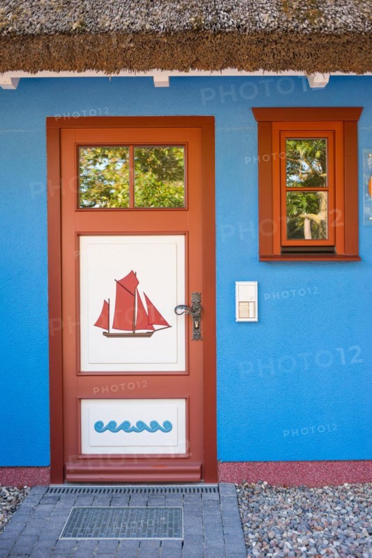 Colourful front door in brown, white and blue with a sailing ship as a motif and matching window frames in the blue wall of a thatched house, thatched roof, historic wooden door with carvings, maritime, artists' village Baltic resort Ahrenshoop, Fischland, Fischland-Darß-Zingst peninsula, Baltic Sea, Mecklenburg-Western Pomerania, Germany, Europe