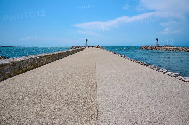 A long concrete path leads to the sea, flanked by breakwaters under a sunny, cloudy sky, summer, Le Grau-du-Roi, Gard, Mediterranean, France, Europe