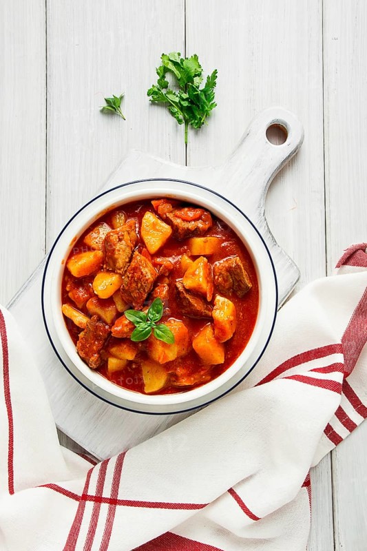 Potatoes stewed with meat, in tomato sauce, with spices and herbs, no people, on a white table