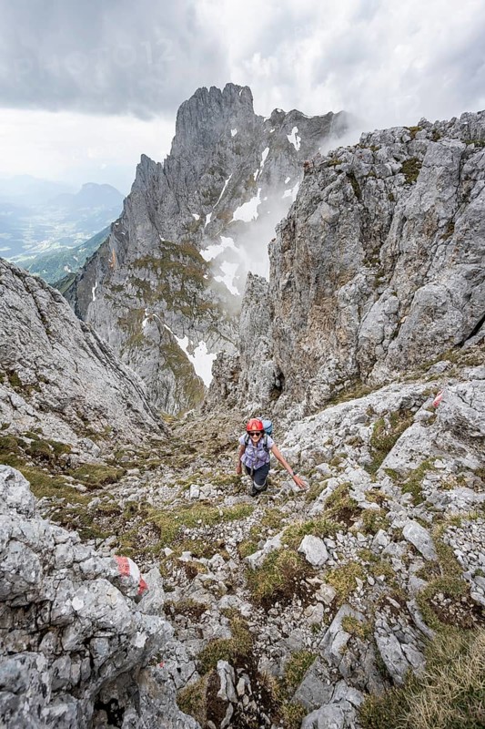 Mountaineer with helmet on a narrow hiking trail, ascent to the Maukspitze, clouds moving around the mountains, Ackerlpitze in the background, Wilder Kaiser, Kaiser Mountains, Tyrol, Austria, Europe