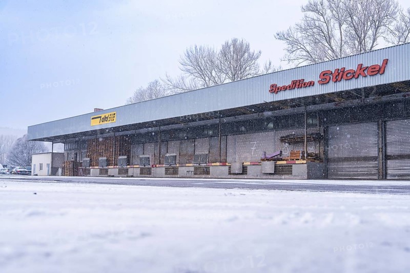 Snow-covered warehouse under cloudy skies with lorry loading, Nagold, Black Forest, Germany, Europe