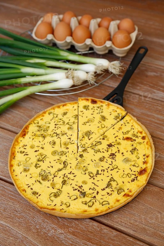 Swabian cuisine, salted cream cake with spring onions, hearty cake, salty short pastry, baked, out of the oven, baked goods, spring onions, winter onions, cooling rack, cake rack, pan lifter, spatula, vegetarian, typical Swabian reinterpreted, baking, wooden stirring spoon, cooking spoon, wooden plate, eggs, fresh chicken eggs in egg carton, traditional cuisine, food photography, studio, Germany, Europe