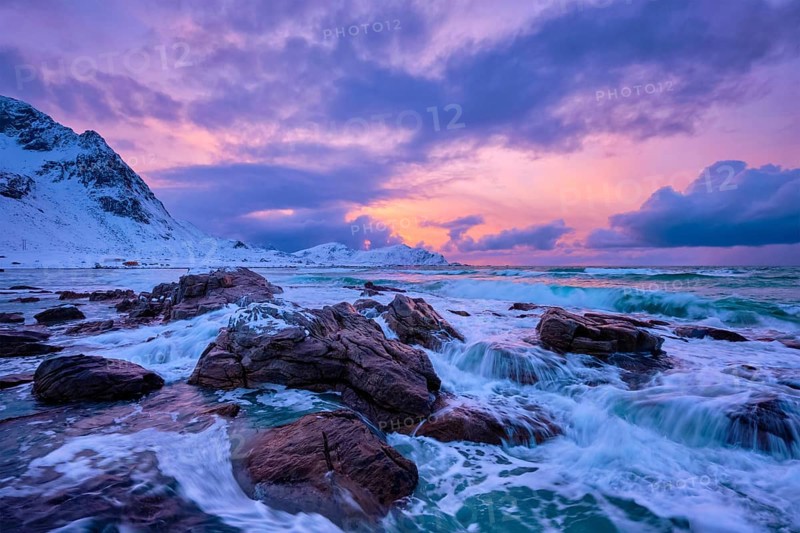 Waves of Norwegian sea on rocky coast in fjord on sunset with sun. Skagsanden beach, Lofoten islands, Norway, Europe