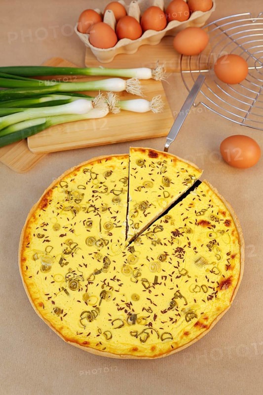 Swabian cuisine, salted cream cake with spring onions, hearty cake, salty shortcrust, baked, out of the oven, baked goods, spring onions on wooden board, cutting board, winter hedge onions, cooling rack, cake rack, cake shovel, cake ladle, vegetarian, typical Swabian reinterpreted, baking, wooden stirring spoon, cooking spoon, eggs, fresh chicken eggs in egg carton, traditional cuisine, food photography, studio, Germany, Europe
