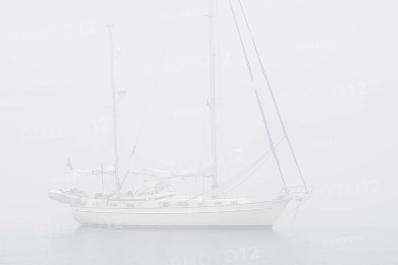 Sailboat, sailing boat, yacht with lowered sails anchored at sea during bad visibility due to thick fog, dense mist
