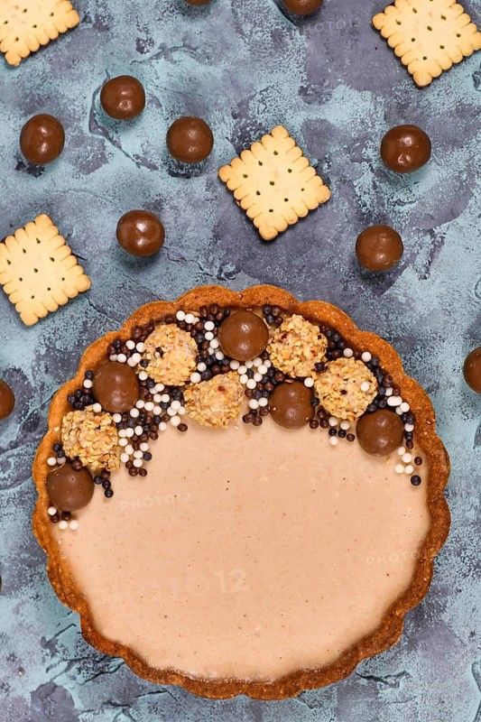 Top view of sweet tart with cheesecake milk chocolate cream filling topped with pralines and chocolate sprinkles
