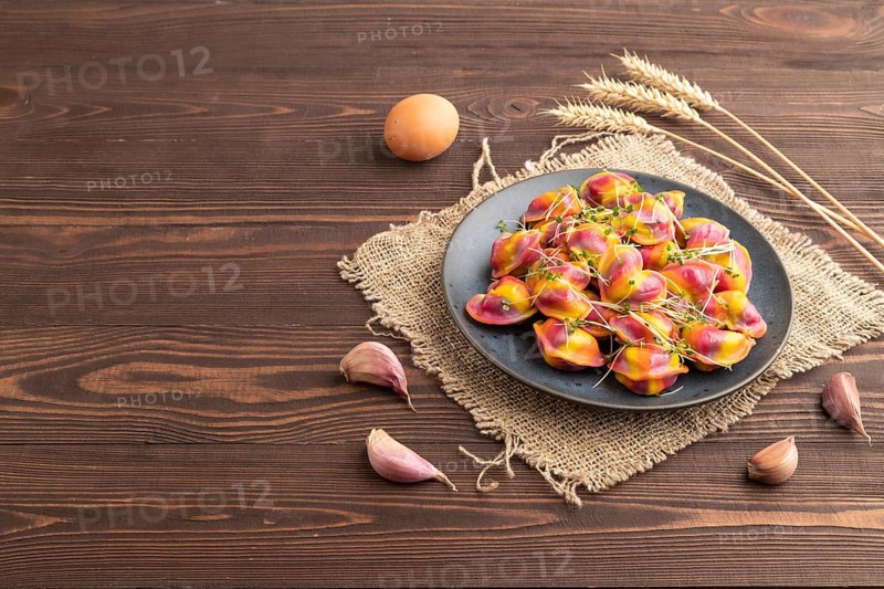 Rainbow colored dumplings with pepper, herbs, microgreen on brown wooden background and linen textile. Side view, copy space