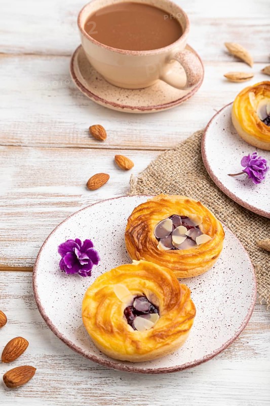 Small cheesecakes with jam and almonds with cup of coffee on a white wooden background and linen textile. Side view, close up