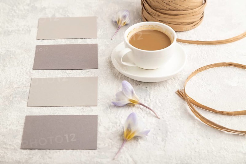 Gray paper business card mockup with spring snowdrop crocus flowers and cup of coffee on gray concrete background. Blank, business card, side view, copy space, still life. spring concept