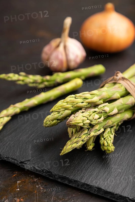 Bunch of fresh green asparagus, garlic, onion on slate board on black concrete background. Side view, close up, selective focus. harvest, healthy, vegan food, concept