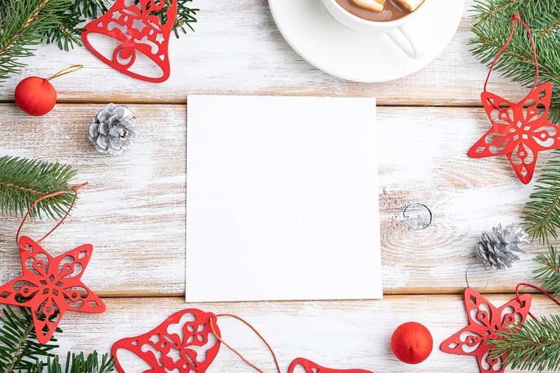 Christmas or New Year frame composition, template. Decorations, red stars, bells, cones, fir and spruce branches, cup of coffee, on a white wooden background. Top view, copy space, flat lay