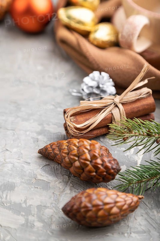 Christmas or New Year composition. Decorations, cones, cinnamon, fir and spruce branches, cup of coffee, wool scarf on a gray concrete background. Side view, copy space
