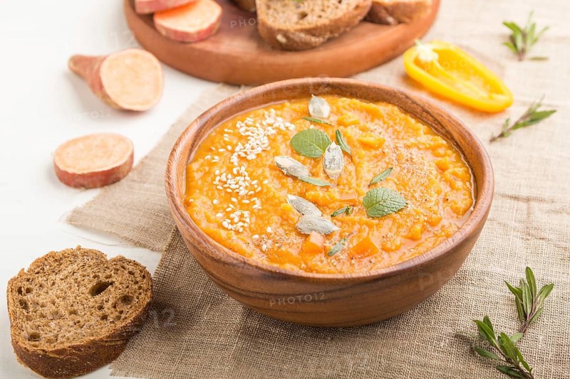 Sweet potato or batata cream soup with sesame seeds in a wooden bowl on a white wooden background with linen textile. side view, close up, selective focus