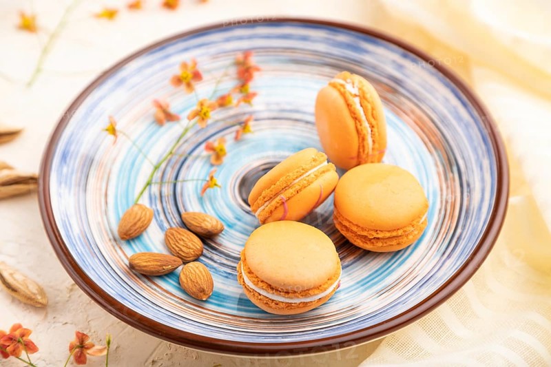 Orange macarons or macaroons cakes with cup of coffee on a white concrete background and linen textile. Side view, close up, selective focus