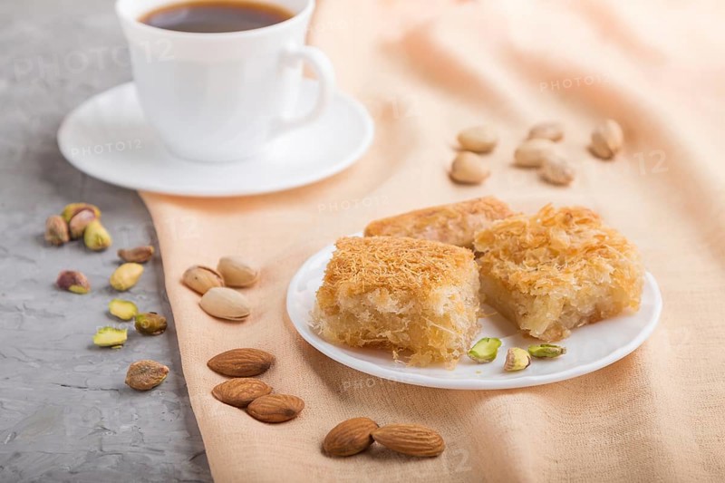 Traditional arabic sweets (basbus, kunafa, baklava) and a cup of coffee on a gray concrete background and orange textile. side view, close up, selective focus