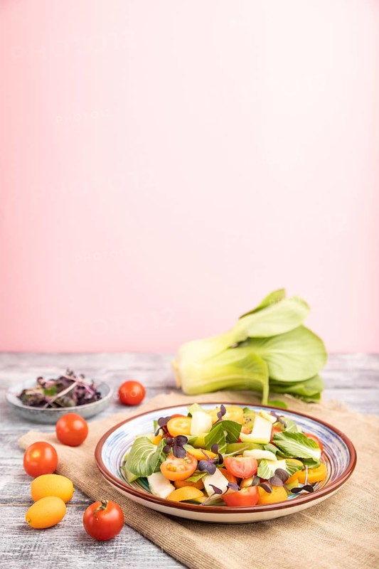 Vegetarian salad of pac choi cabbage, kiwi, tomatoes, kumquat, microgreen sprouts on gray and pink background and linen textile. Side view, close up, selective focus, copy space
