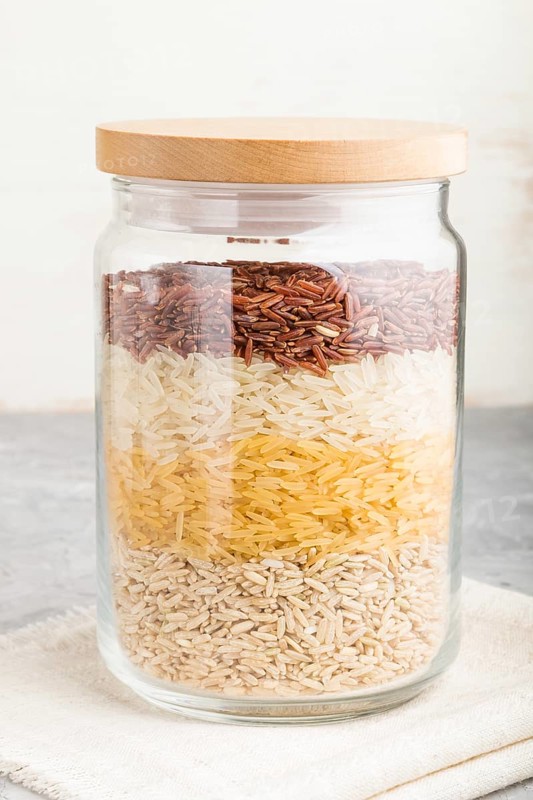 Glass jar with different kinds of rice poured in layers on a gray and white background. side view, close up. Healthy food concept